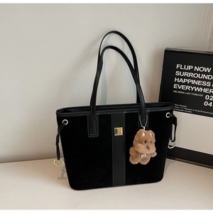 Detail of black suede tote bag with golden buckle and cute plush dog charm accessory