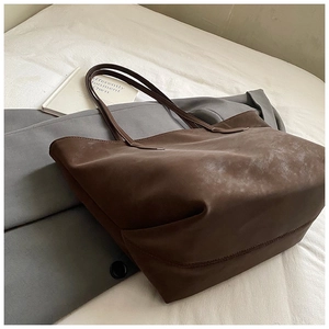 Large dark brown tote bag on white bed with grey suit jacket and a book