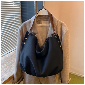 Close-up of black tote bag with brown leather strap and silver rivet accents