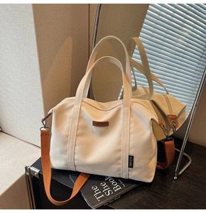 Detail of canvas tote bag with brown leather logo patch and orange woven shoulder strap