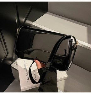 Detail of glossy black patent leather baguette bag with gold metal hardware on grey steps