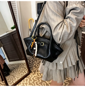 Detail of black vintage leather handbag with colorful wooden bead tassel and gold buckle