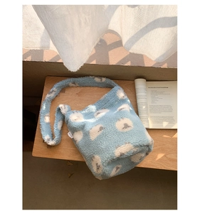 Détail du sac seau bleu clair en peluche avec motif mouton sur une surface en bois
