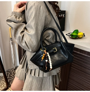 Detail of a black faux leather crossbody bag with wooden bead tassels and gold buckle