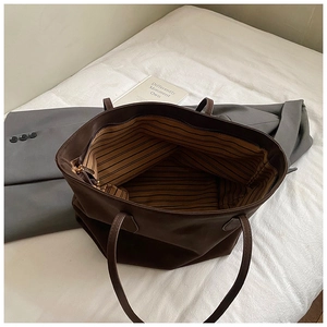 Close-up of a large coffee brown tote bag showing striped lining and zipper closure detail
