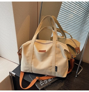 Close-up of beige canvas tote with orange leather logo and adjustable shoulder strap