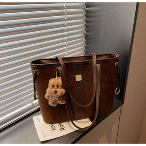 Detail of a brown suede tote bag with leather straps and a plush dog charm by the window