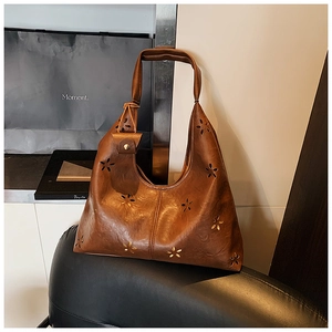 Détail du sac hobo en cuir marron avec motifs floraux découpés au laser et rivets