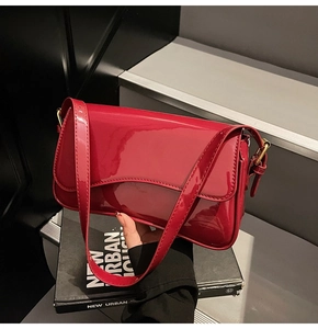 Detail of red patent leather baguette bag with wavy flap design and gold hardware