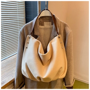 Close-up of beige canvas tote with brown leather strap and rivet detailing on a coat
