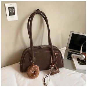 Detail view of brown faux suede Boston bag with donut and heart bag charms on a desk