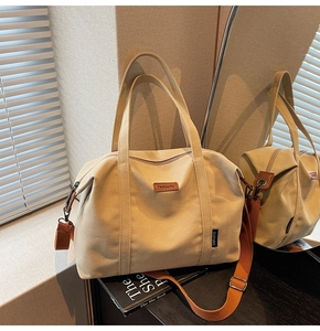 Detail of beige canvas tote bag with adjustable orange strap and leather brand label