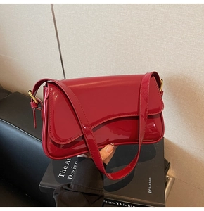 Detail of red patent leather shoulder bag with glossy finish and golden metal buckle