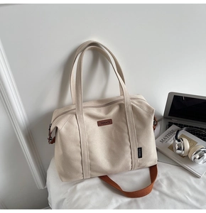 Detail of minimalist canvas tote with leather brand tag, laptop, and artistic books