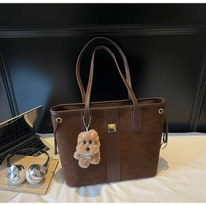 Close-up of a dark brown suede tote bag with a cute plush dog charm and laptop