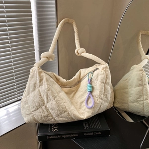 Detail of cream quilted hobo bag with knotted shoulder strap and colorful braided charm