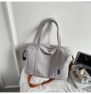Light gray canvas tote bag with brown leather logo tag and orange strap for commuting