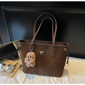 Detail of a brown suede tote bag with leather straps, gold accents and a plush dog charm