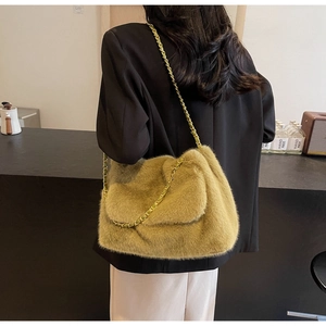 Détail du sac à bandoulière en peluche jaune moutarde avec chaîne dorée sur fond sombre