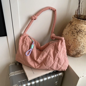 Detail of dusty pink quilted tote bag with knot handle resting on a suitcase