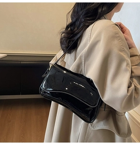 Side view of a black patent leather shoulder bag worn with a khaki trench coat