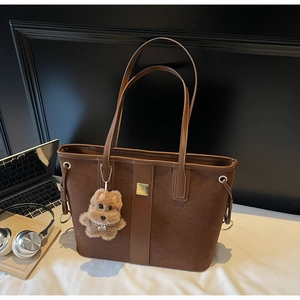 Detail of dark brown suede tote bag with metal buckle and plush puppy charm accessory