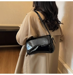 Detail view of black patent leather shoulder bag with gold buckle on a stylish model