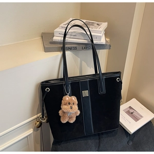 Detail of black suede tote bag with vertical stripes and a brown teddy bear charm