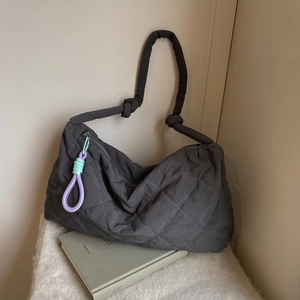 Detail of black quilted cloud bag featuring braided rope knots and colorful zipper pendant