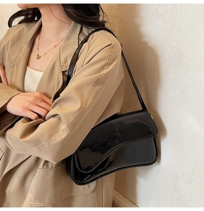 Detail of black glossy patent leather shoulder bag with sleek flap and luxury mirror finish