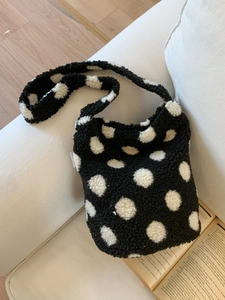 Sac seau en peluche à pois noir et blanc posé sur un canapé beige minimaliste