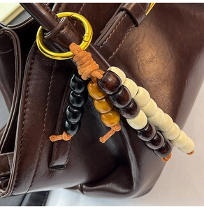 Detailed close-up of ethnic beaded charm with golden metal ring on a leather handbag