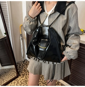 Detail of glossy black pleated shoulder bag featuring a gold metallic arc buckle
