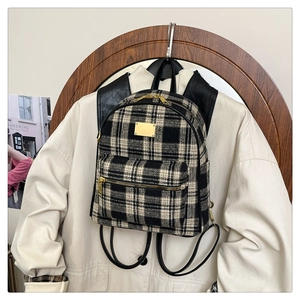 Détail d'un sac à dos à carreaux noir et blanc avec double fermeture éclair dorée et cuir