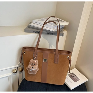 Close-up of brown suede patchwork tote bag with metal buckle and plush puppy charm