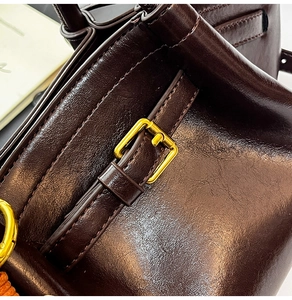 Detailed close-up of dark brown leather texture and gold-tone metal side buckle of the bag