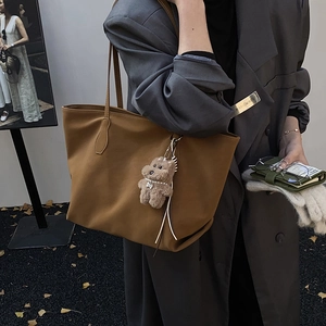Retro brown leather tote bag with plush bear charm worn by a model in a grey suit