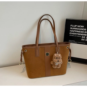 Detail of brown suede tote bag with leather straps and a cute plush bear keychain charm