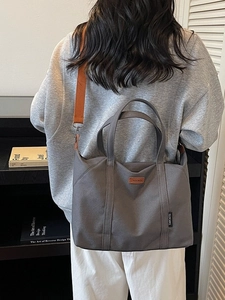 Dark grey canvas tote bag with orange shoulder strap shown in a lifestyle casual setting