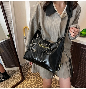 Detail of black glossy shoulder bag with gold crescent buckle on a model wearing stripes