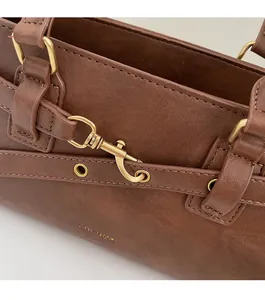 Close-up of golden hardware connectors and textured brown leather on underarm bag