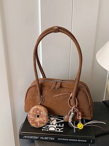 Vintage brown underarm Boston bag with long handles and plush charms on a book background