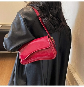 Close-up of a red patent leather shoulder bag with gold buckles worn by a model