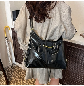 Detail of black glossy faux leather shoulder bag with gold hardware and stylish side pleats