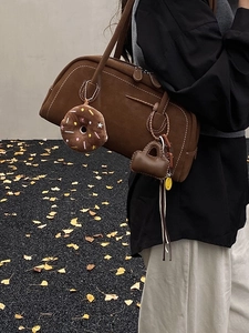 Vintage brown suede Boston shoulder bag with plush charm on a model with autumn leaves
