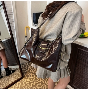 Detail view of deep brown glossy leather tote bag with elegant gold curved metal hardware