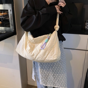 Close-up of cream quilted shoulder bag with knotted strap and colorful tassel on model