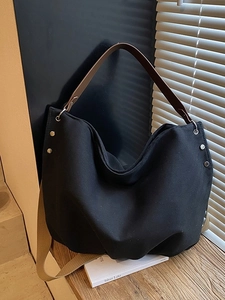 Minimalist black canvas tote bag with adjustable straps on a rustic wooden table