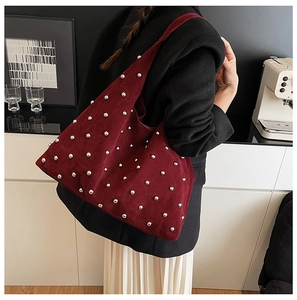 Detail shot of burgundy suede shoulder bag with silver rivet studs on textured fabric