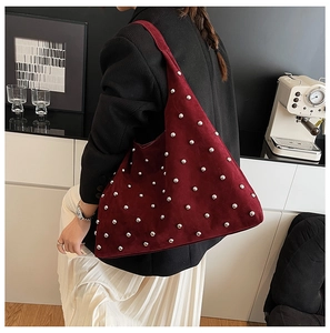 Detail of burgundy suede shoulder bag featuring silver stud rivets and a modern hobo shape